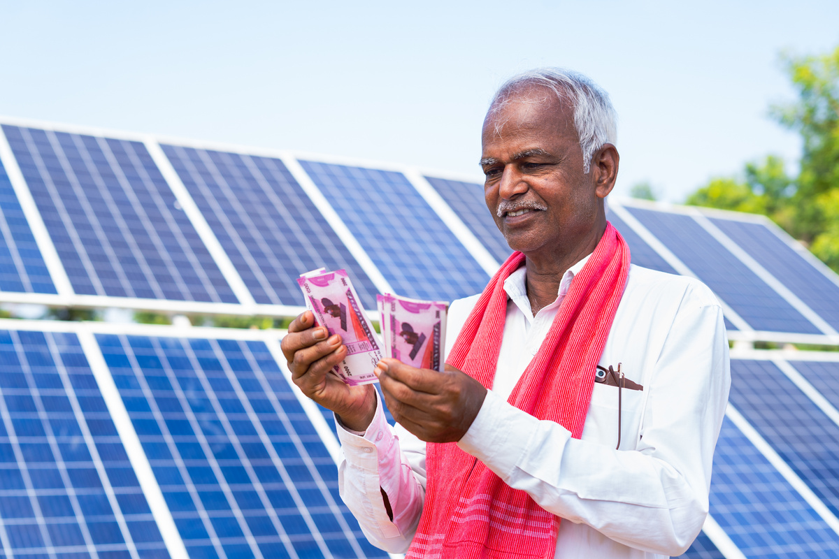 Happy farmer counting money or currency notes in front of solar panel at farmland - concept of loan approval, bank subsidy and savings or investment.